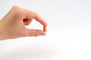 Bir kadın eli iki parmağıyla turuncu bir hap tutuyor. Mesaj için yer. İlaç, ilaç, konsept.
