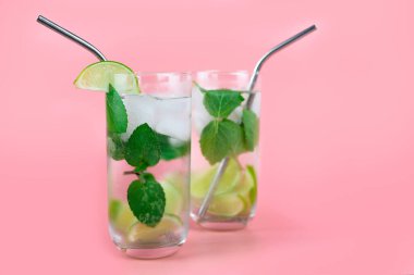 Alkollü kokteyl ya da alkolsüz mojito taze naneli ve limonlu ve pembe arka planda çevre dostu pipetli insanlar. Metin için yer.