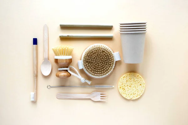 Eco-friendly biodegradable disposable cutlery, cups, sponge, cotton string bag and dishwashing brush on a beige background. Zero waste. Environmental pollution. Place for text