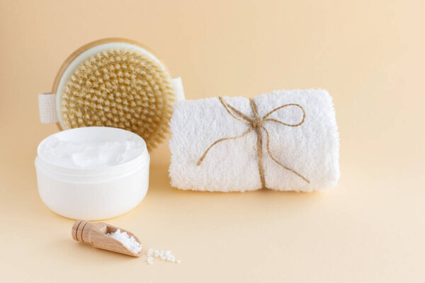 The concept of body and skin care at home. Sea salt scrub, cream, massage brush and white terry towel.