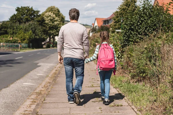 Back to school. A dad, father or parent accompanies or leads a daughter with a backpack or knapsack to school down the street and holds her hand. first day of school, new school year. — Stock Photo, Image
