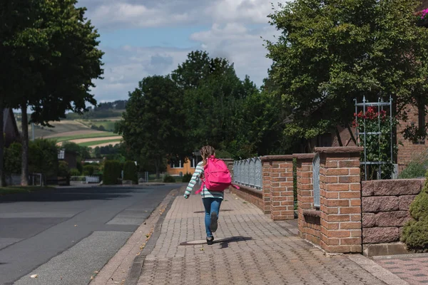 A girl with a pink satchel on her back runs down the street to school. The first day of school, the children are ready to study after the holidays