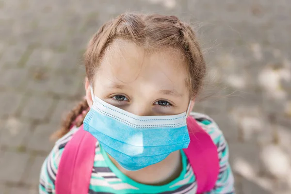 Yüzünde koruyucu bir maske olan okul çağındaki bir kızın yakın plan portresi. 2020 'de yeni okul yılı. Eğitim kurumlarında koronavirüs döneminde çocukların korunması.