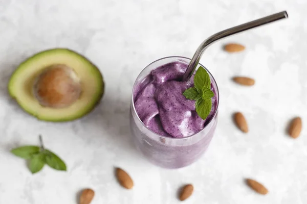 Summer refreshing smoothie with avocado, blueberries and almond milk in a glass glass with a reusable iron straw on a light background. Diet cocktail, keto recipes