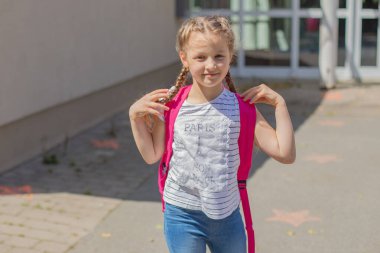 Tecritten ya da tatilden sonraki ilk okul gününde okul bahçesinde sırtında sırt çantası olan sevimli bir kız. Çocuklar okula döndükleri için mutlular..