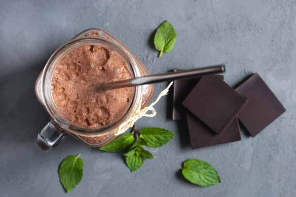 An overhead view of a Chocolate smoothie, cocktail, almond milk and cream drink in a glass jar with a reusable iron straw and mint leaves and chocolate pieces