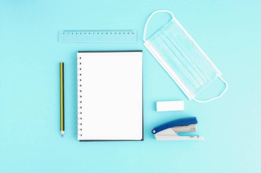 Boş çarşaflı boş bir defter, kırtasiye malzemesi, koruyucu maske, zımba, cetvel, kalem. Karantina ve virüs süresince metin, ofis işleri için yer.