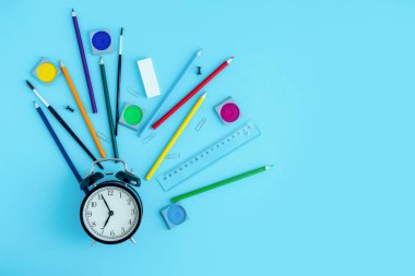 Kırtasiye malzemeleri, pastel boyalar, fırçalar ve siyah alarmlı saatin etrafındaki boyalar. Okula dönüyorum, okul yılına başlıyorum. Boşluğu kopyala