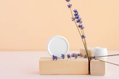 Kurumuş lavanta çiçeklerinin yanında beyaz bir yüz ya da vücut kremi kavanozu. Doğal bakım kozmetik konsepti. Metin için yer.