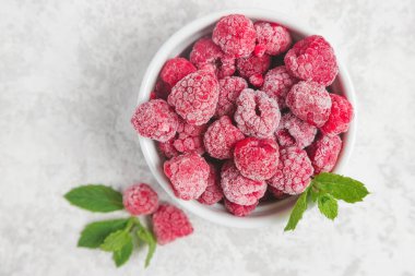 Top view of a bowl full of frozen raspberries with mint leaves. Eating, buying and storing frozen berries. clipart