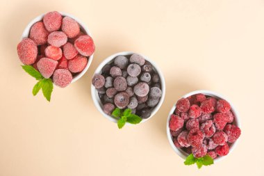 Frozen blueberries, strawberries and raspberries in bowls on a neutral background. Freezing food. Long-term storage. Copy space clipart