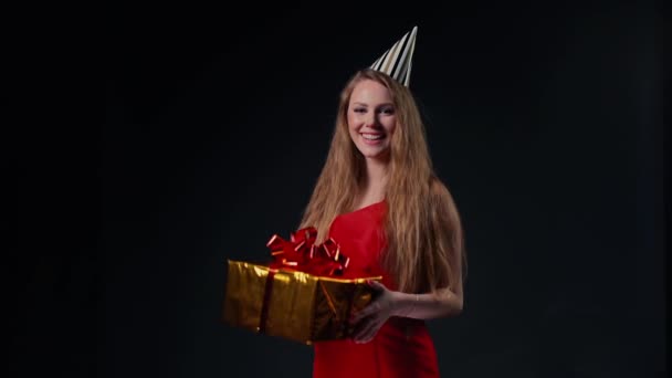 Aranyos fiatal nő ünnepi sapkában tart egy ünnepi dobozt ajándékkal.