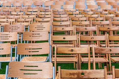 Bir sürü ahşap sandalye yağmurda parkın dışında duruyor. Boş oditoryum, yeşil çimenler, ağaçlar ve su damlaları ile sandalyeler.