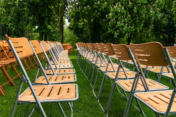 Lot of wooden chairs stand outside in the park in the rain. Empty auditorium, green grass, trees and chairs with water drops.