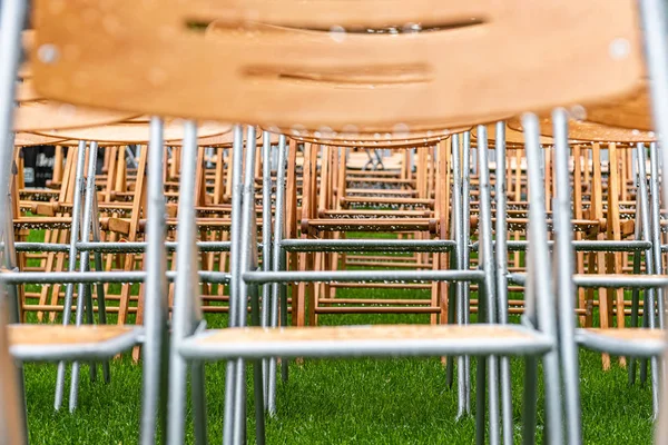 Lot of wooden chairs stand outside in the park in the rain. Empty auditorium, green grass, trees and close-up chairs with water drops.