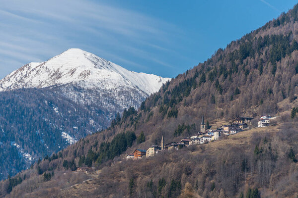 Spring in Italy, sun, cloudy sky and snow covered mountains. View on Termenago - small Italian village near Ski region Val di Sole, Alps, Trento, Italy, Europe