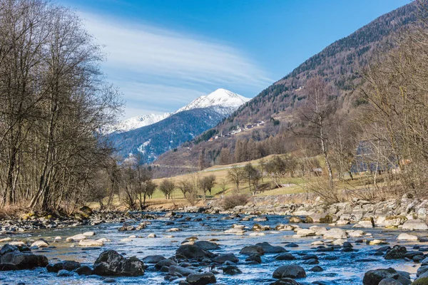 Italian mountain river called Noce River. View of snow covered mountains and Termenago - small village near Ski region Val di Sole, Italy, Europe