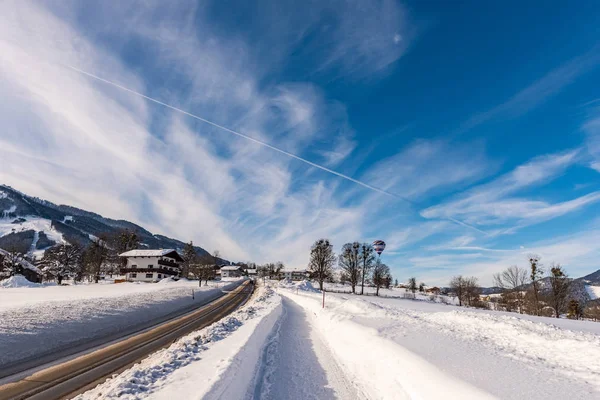 Blue cloudy sky, big snow covered fields and empty road in winter, sunny day.