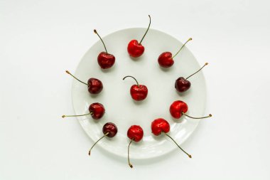 Kırmızı tatlı kiraz beyaz bir plaka üzerinde yatıyor, bir izolatör