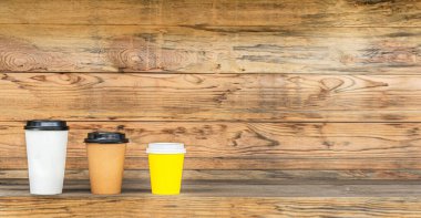 Kahve için üç tane renkli kağıt bardak ahşap bir arka planda ve ahşap bir masada..