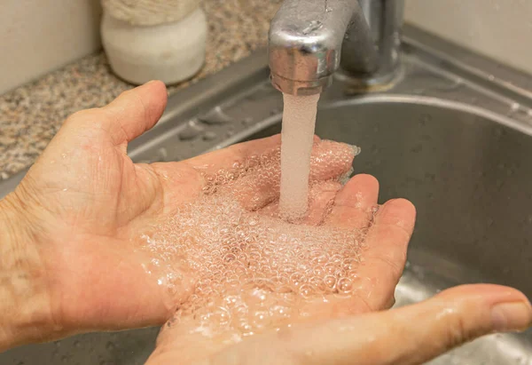 On the hands of an elderly woman, water flows from a shiny faucet. Water is bubbling. Close-up. Coronovirus protection. Personal hygiene.