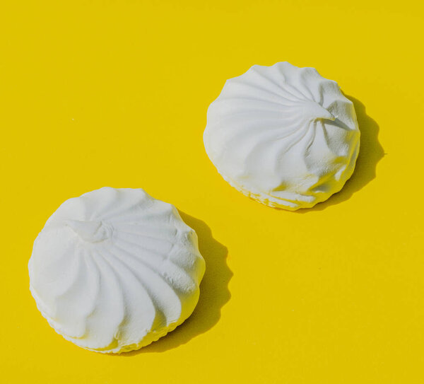 White, delicate, soft marshmallows are located on a yellow background and have sharp shadows. Sweets are needed for joy