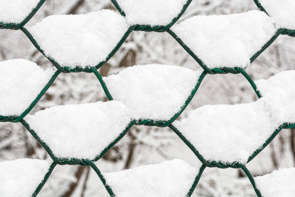 Close-up of a metal chain-link fence with adhering white snow.