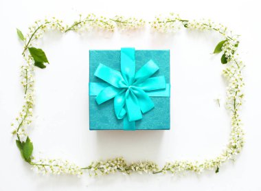 Mavi kurdele ve beyaz arka plan üzerinde beyaz çiçeklerden yapılmış yuvarlak çerçeve ile mavi hediye kutusu. Noel, Sevgililer Günü veya doğum günü konsepti. Metin için yer. Üst görünüm, düz yatıyordu. Çiçek kompozisyonu. 