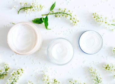 Beyaz arka plan üzerinde kozmetik ürünler ve çiçekler ile Düz yatıyordu kompozisyon. Nemlendirici krem ile kase seti. Metniniz veya logonuz için yerleştirin. Çeşitli yüz kozmetik ürünleri. Güzellik arka plan.