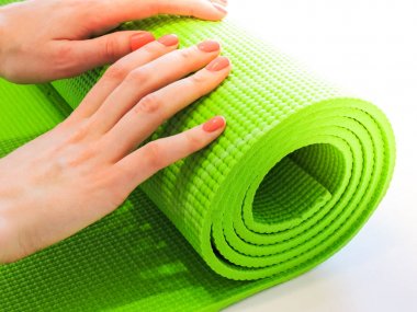 Egzersiz sonrası yoga minderini yuvarlayan bir kadın. Güzel bir bakış açısı. Sağlıklı yaşam, formda konseptler. Üstteki yeşil yoga paspas sporu izole edildi. Yoga minderini sarıp beyaza sarmaladık. Kopyalama alanı.