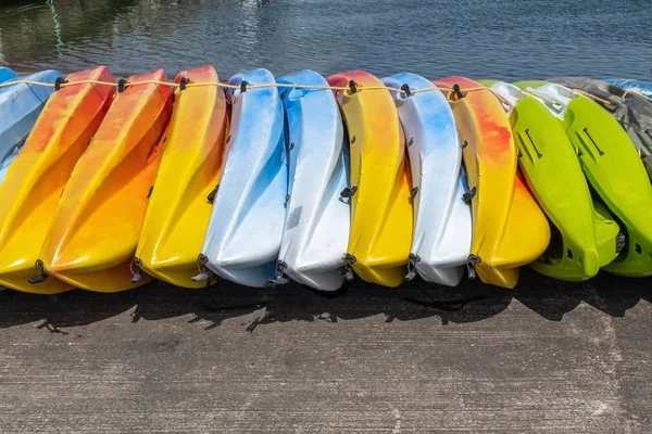 Una fila de kayaks de colores brillantes sentados en el suelo, colores incluidos verde amarillo y azul — Foto de Stock