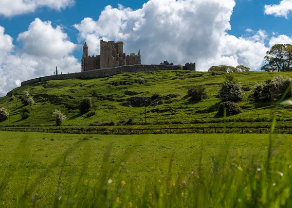 Widok na zielone pola do wspaniałej skały Cashel i kamiennej twierdzy i opactwa, przed jasnym błękitne niebo i Puszyste białe chmury — Zdjęcie stockowe