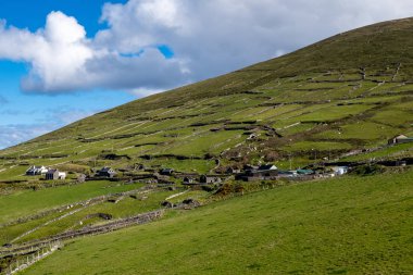 Dingle Yarımadası'ndaki Slea Head Viewpoint'ten küçük yerleşimlere vadiboyunca bakmak, İrlanda, kabarık bulutlu parlak mavi gökyüzü