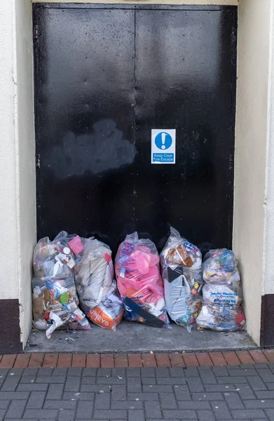 Kilkenny, Irlanda, 10 de mayo de 2019: Bolsas de bolsas de plástico transparente se amontonan en una puerta que es una salida de incendios — Foto de Stock