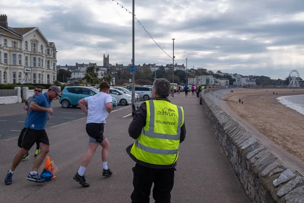 Exmouth, Devon, Regno Unito, 13 aprile 2019: Correre partecipando a un evento Park Run sul lungomare di Exmouth, volontario in primo piano per assicurarsi che i corridori stiano bene — Foto Stock