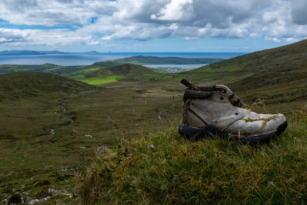 Оглядываясь назад к Динглу с вершины перевала Конор на полуострове Дингл, Ирландия, яркое голубое небо с пушистыми облаками, старый заброшенный ботинок на переднем плане — стоковое фото