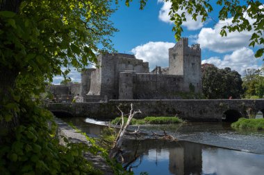 A view of the Castle of Cahir across the weir down the River Suir, bright blue sky and fluffy white clouds clipart