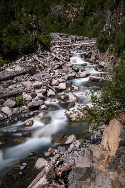 Un río poco profundo en el borde de un Parque Nacional en EE.UU., larga exposición para crear desenfoque de movimiento en el agua, ya que cae en cascada sobre rocas y árboles caídos — Foto de Stock