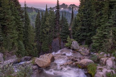 Bir şelalenin tepesinden dağların bir dizi gün batımında bir görünüm, gökyüzü kırmızımsı bir renk ve dağlarda kar kapalı parlar