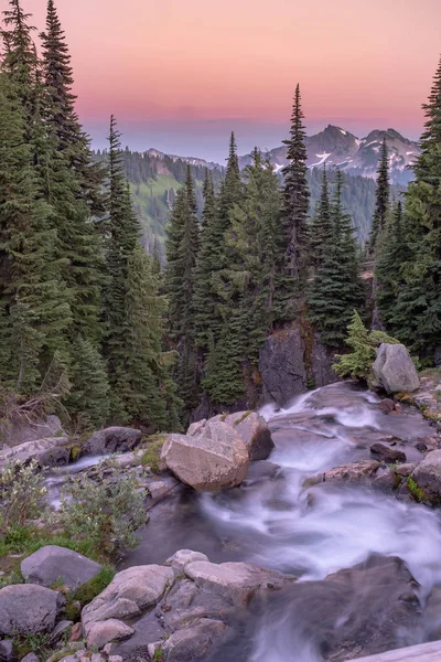 Портретний вид на захід сонця різноманітних гір з вершини водоспаду, небо червонуватого кольору і відбиває сніг на горах — стокове фото