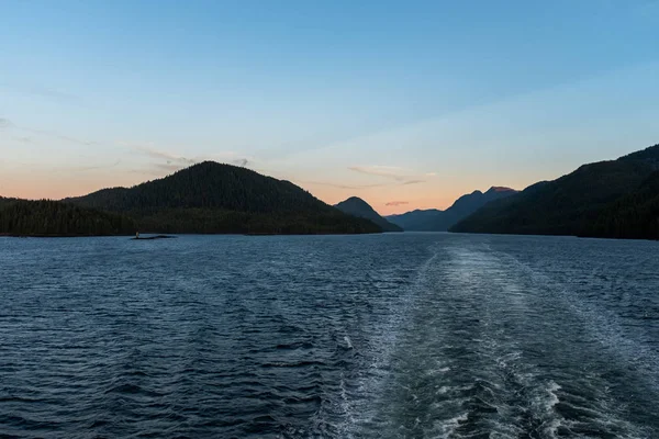 Η θέα στο ηλιοβασίλεμα από το πίσω μέρος ενός φεριμπότ καθώς περνά μέσα από το εσωτερικό πέρασμα από την άγρια δυτική ακτή του Καναδά, το φως που ξεθωριάζει στην απόσταση — Φωτογραφία Αρχείου