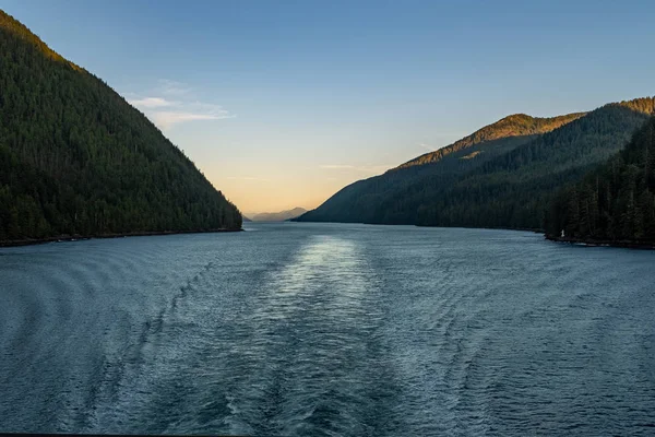 A vista no por do sol da parte traseira de um ferry enquanto faz sua maneira através da passagem interna fora da costa ocidental áspera de Canadá, a luz que desvanece-se atrás das colinas na distância — Fotografia de Stock