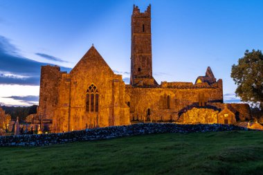 Quinn ortaçağ Quinn Abbey kalıntıları bir yan görünümü, İrlanda görüntüde manastır kimse giden patika aşağı bakarak, derin bir mavi günbatımı gökyüzüne karşı aydınlandı