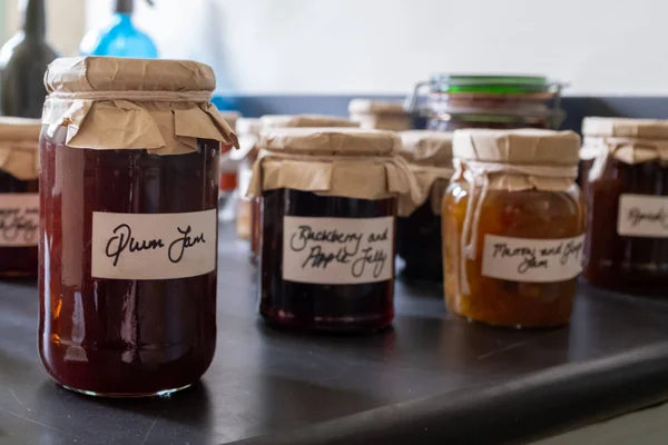 Mehrere Gläser hausgemachte Marmelade auf einer Arbeitsplatte sitzend, mit altmodischem braunem Papier und Fadendeckeln mit handgeschriebenen Etiketten, das erste Glas im Fokus und der Rest unscharf — Stockfoto