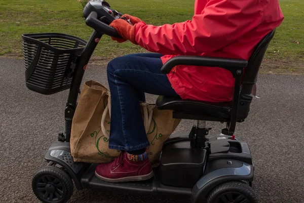 Un lado en la toma de una anciana con un abrigo rojo disfrutando de la libertad de un scooter de movilidad eléctrica . — Foto de Stock