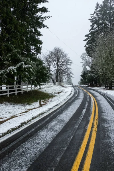 Uma estrada levemente coberta de neve nos arredores de Portland, Oregon, EUA, as linhas amarelas duplas que levam à distância — Fotografia de Stock