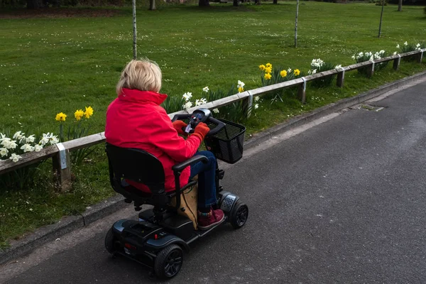 Kırmızı bir ceket bir yaşlı Bayan çiçek bahar nergis ile sessiz bir yolda bir elektrikli hareketlilik scooter özgürlüğü zevk.