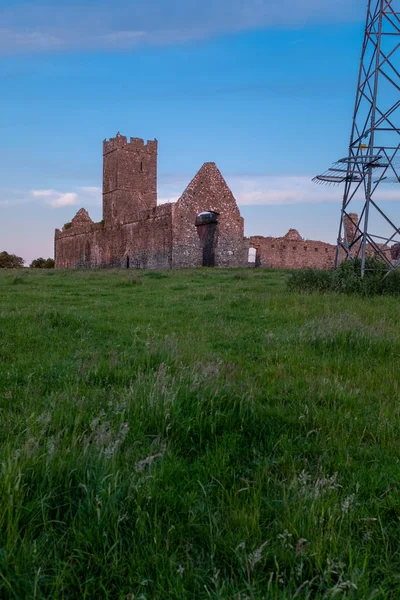 Vista do retrato das ruínas da Abadia de Clare um mosteiro agostiniano nos arredores de Ennis, Condado de Clare, Irlanda ao pôr-do-sol com o fundo de um pilão de energia em primeiro plano — Fotografia de Stock