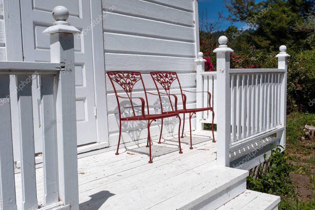 Two red  ornate metal chairs on a white wooden porch