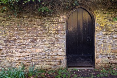 Duvarlı bir bahçeye giden kuru bir taş duvarda siyah bir kapı. 